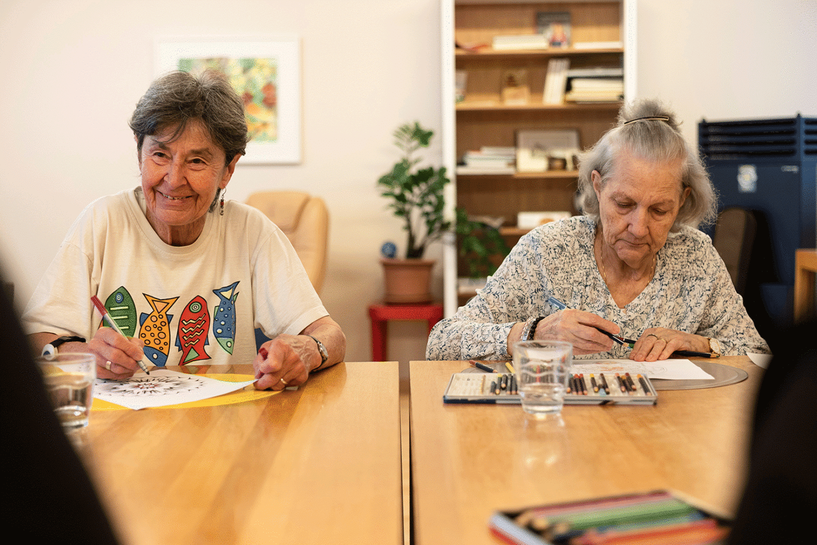 Zwei ältere Damen sitzen an einem Tisch und malen.